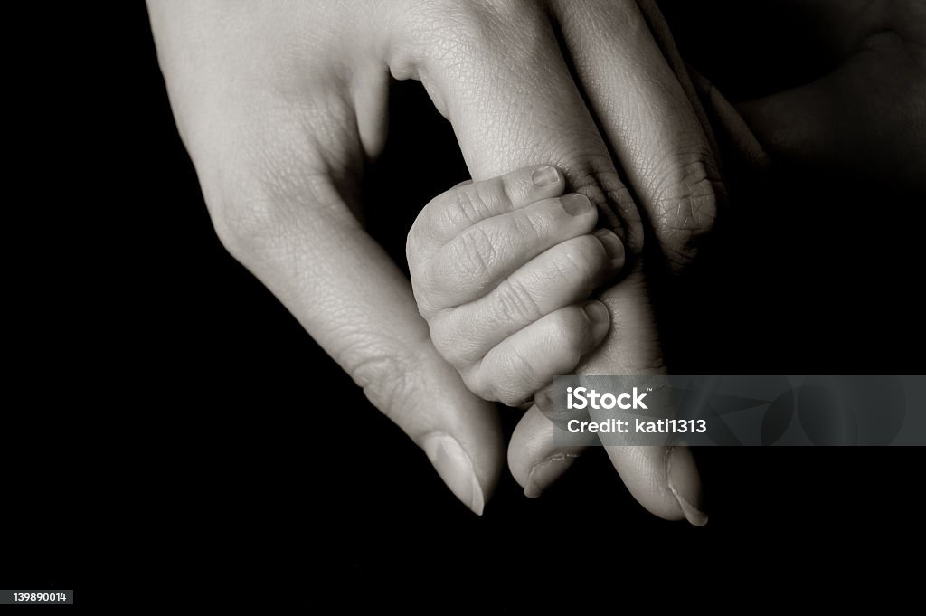 Hand holding a tiny baby's hand on isolated black background hand of a 11 days young baby Affectionate Stock Photo