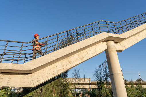 An Asian female worker stands on the stairs of a viaduct and uses a computer