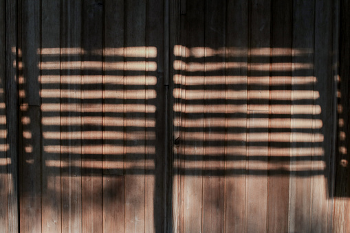 Shadows and sunlight on a brown wooden wall. Beams of sunlight through old window wooden blinds.