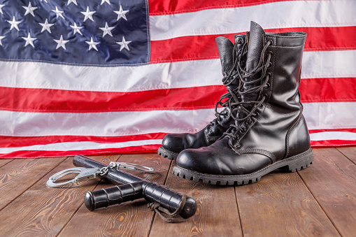 USA military boots, hat and dog tags with American flag in background.  No people in this US Memorial Day or Veteran's Day image.