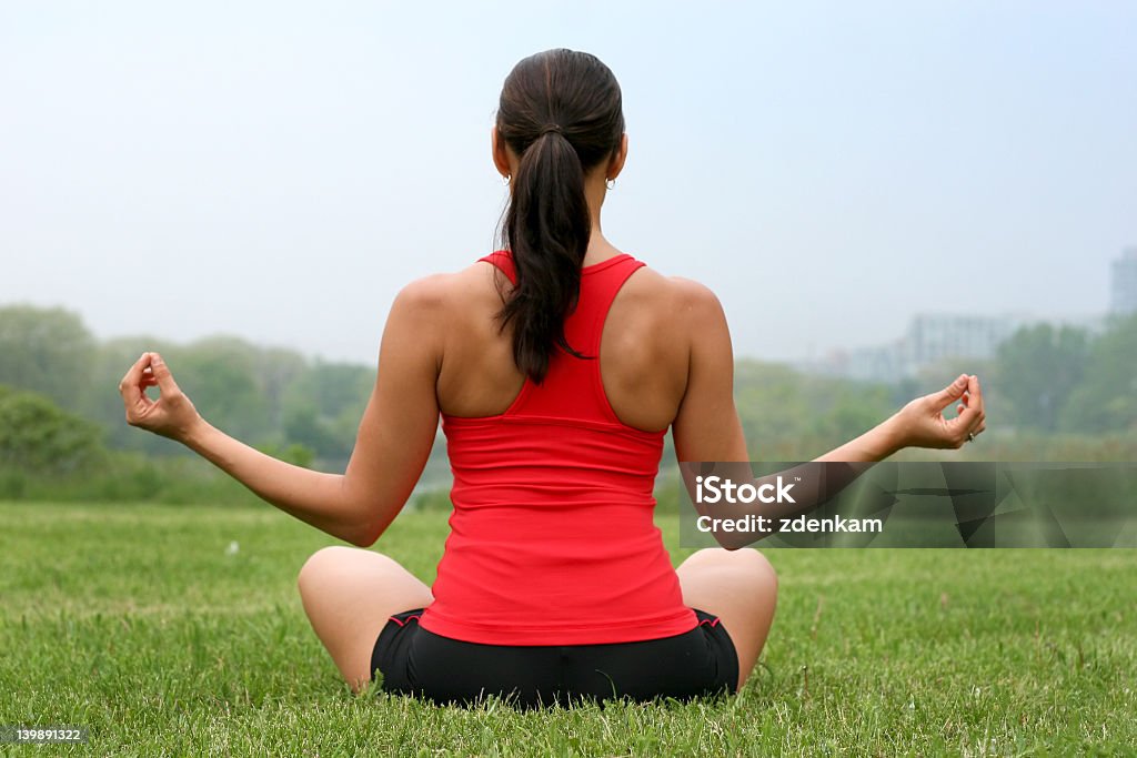 A female yoga instructor sitting in a grass field beautiful brunette doing her yoga wearing sport wear Active Lifestyle Stock Photo