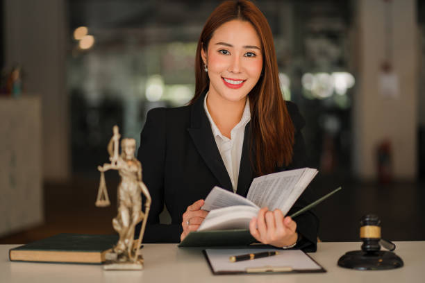 Attractive Asian Lawyer Female Lawyer Discussing Contract Documents with Golden Goddess Scales with Hammer on Wooden Tables in Office of Legal Services, Advice, Justice and Real Estate Ideas. stock photo