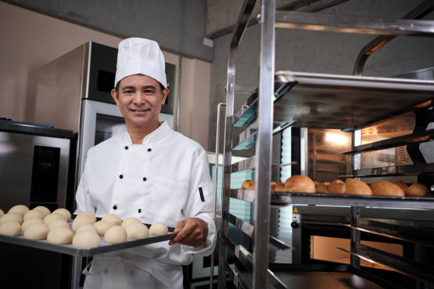 the senior chef showed fresh bread with a smile at the stainless steel kitchen. - buns of steel imagens e fotografias de stock