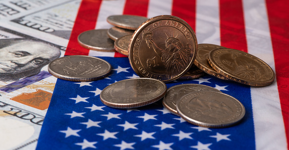 Coins in denominations of 1 US dollar and 25 cents on the background of the American flag