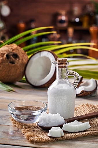 Glass bottle of coconut oil and fresh coconut fruit on wooden rustic white background, alternative therapy medicine concept