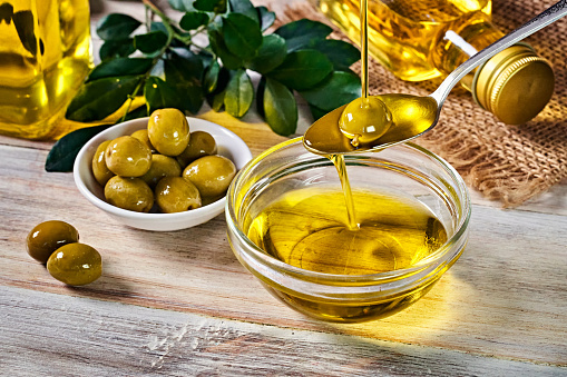 Close-up of pouring olive oil from bottle to spoon and container. Arrange on table in old fashioned rustic kitchen.
