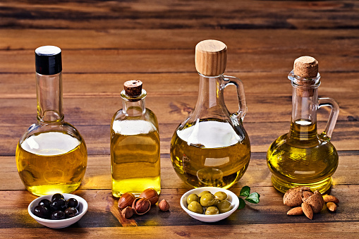 Assorted healthy vegetable oil bottle collection on wooden table in a old fashioned kitchen with low key illumination: Olive oil, hazelnut oil, almond oil and  coconut oil