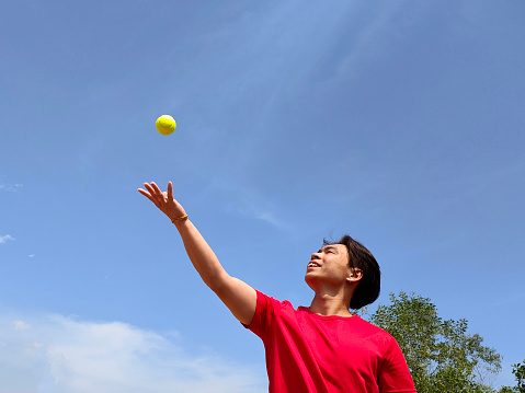 An Asian man is feeling joyful and accomplished while throwing tennis ball in the air.