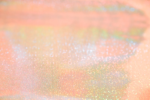 Holographic abstract shiny defocused background with bokeh in pastel orange tones of peach rose gold color