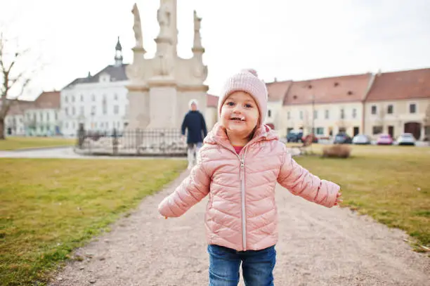 Baby girl with lollipop, wear pink jacket walking at Valtice town, Czech Republic.
