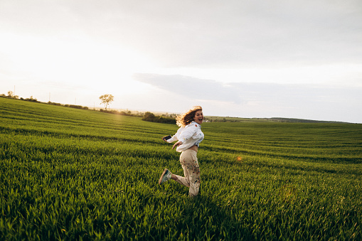 A cheerful woman running on the field and enjoy the moment at the sunset