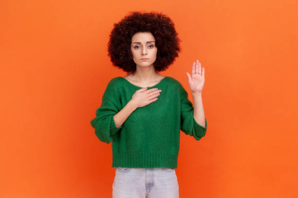 i promise! serious woman with afro hairstyle wearing green sweater standing raising hand and saying swear, making loyalty oath, pledging allegiance. - proof of love imagens e fotografias de stock