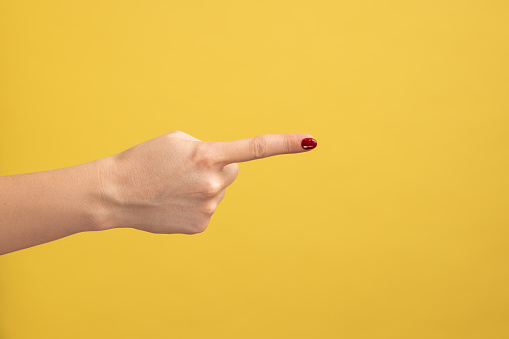 Closeup profile side view of woman hand finger pointing pointing direction to right. Indoor studio shot isolated on yellow background.