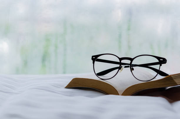 istock Spectacles and book put on bed in morning with rain drop on window. 1398942869