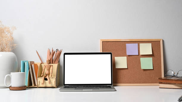 istock Front view mock up laptop computer coffee cup and stationery on white table. Empty screen for advertise text. 1398948074