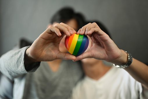 Rainbow heart shape in homosexual couple hands. LGBT, pride, relationships and equality concept.