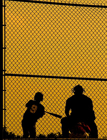 baseball players and umpire sihlouetted against golden sky