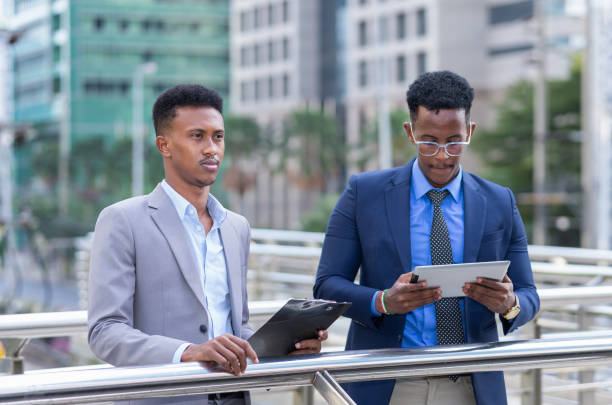 istock black businessman wearing grey suit and working with note, black executive man wearing blue suit, standing and working with tablet outside building in city 1398954206