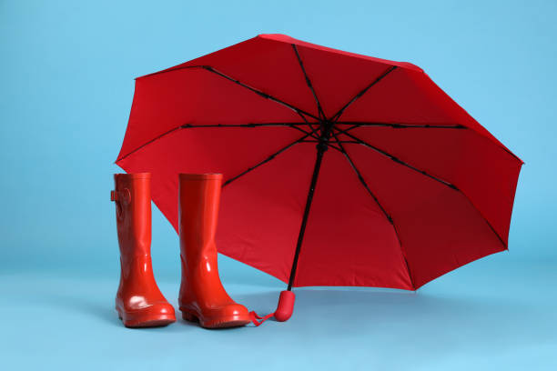 istock Open red umbrella and rubber boots on light blue background 1398954444