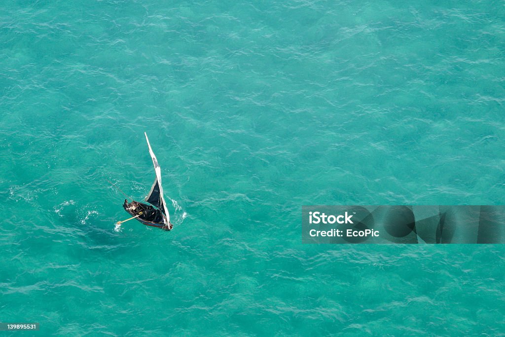 Small sailboat on a teal sea in Mozambique, Africa Aerial view of a small sailboat (called a dhow) on the open sea, Mozambique, southern Africa Mozambique Stock Photo