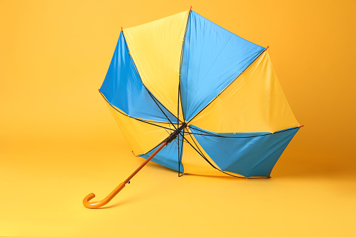 Broken bright umbrella with wooden handle on yellow background