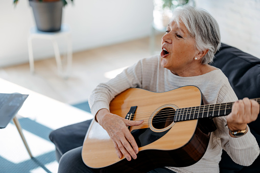 Portrait of beautiful senior woman playing guitar in modern apartment