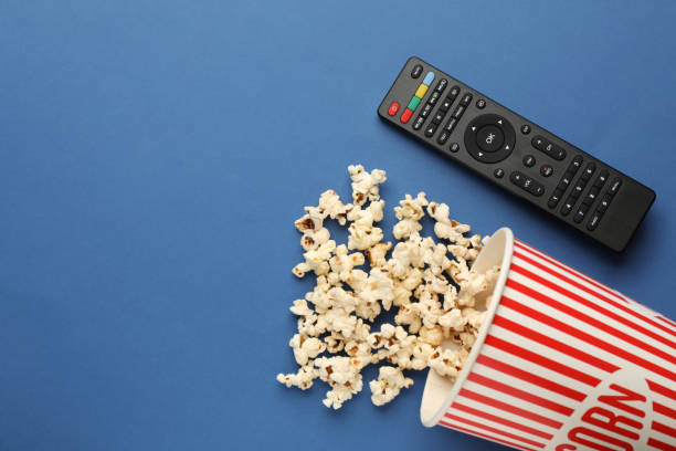 istock Remote control and cup of popcorn on blue background, flat lay. Space for text 1398955823