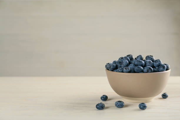 istock Ceramic bowl with blueberries on light wooden table, space for text. Cooking utensil 1398955973