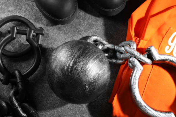 Prisoner ball with chain and jail clothes on grey table, flat lay