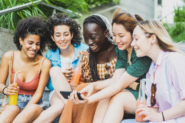 giovani donne diverse che si divertono all'aperto ridendo insieme e utilizzando l'app per smartphone per i social media, concetto di diversità, focus principale sul viso della ragazza africana - solo ragazze foto e immagini stock