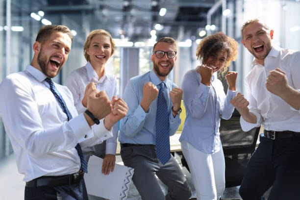 istock Five happy modern business people are keeping arms raised and expressing joyful while standing in large office 1398959894