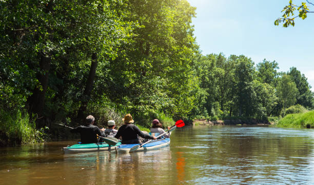Family kayak trip. Man and woman and elderly couple senior and seniora rowing boat on the river, a water hike, a summer adventure. Eco-friendly and extreme tourism, active and healthy lifestyle stock photo