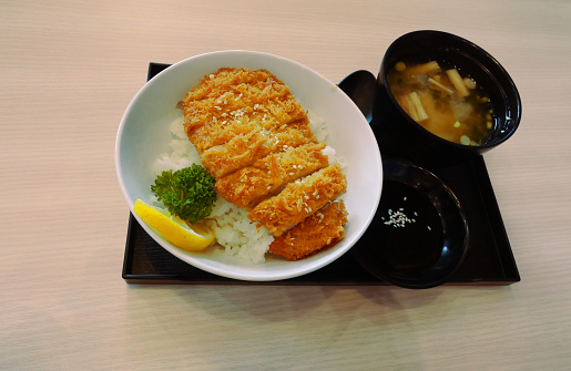 Japanese Katsudon or deep fried Pork on rice in a bowl with miso soup n a black square plate on brown table