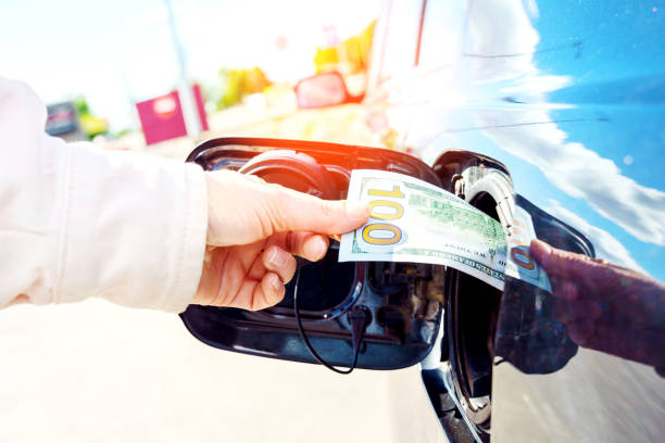 Expensive fuel concept. Rise in fuel price. Hand inserting a hundred dollar bill into the gas tank flap of a car. stock photo