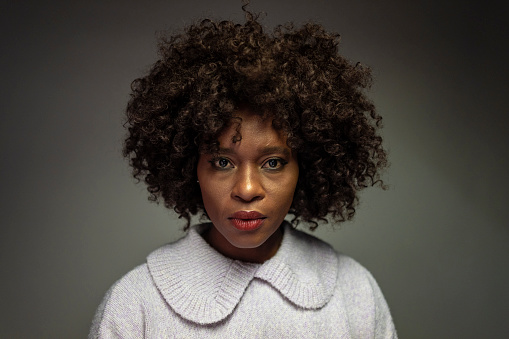 Mature female adult looking straight into the camera with serious emotion wearing a  grey top shot in a studio.