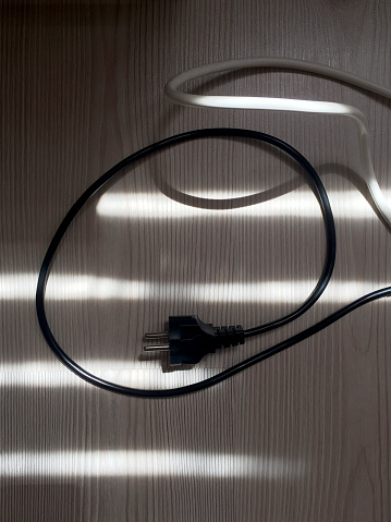 Electric plug on the wooden parquet floor with sunlight reflection and shadow