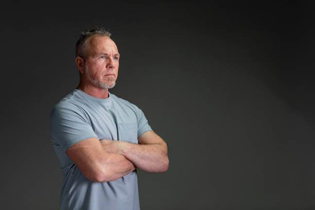 Confident Mature Man A front view waist-up portrait of a fit mature caucasian man standing in front of a grey background with his arms crossed and a confident face looking away from the camera. attraction studio photography stock pictures, royalty-free photos & images