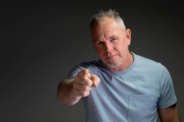 Mature Male Adult Pointing at Camera A front view waist-up portrait of a mature caucasian man standing in front of a grey background pointing towards the camera with a confident look on his face. attraction studio photography stock pictures, royalty-free photos & images