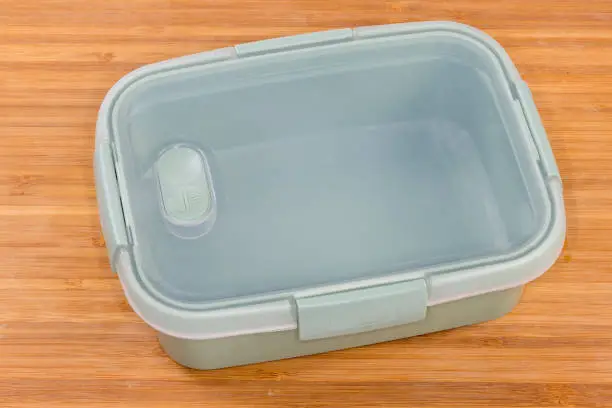 Reusable empty plastic food storage container with closed transparent lid on the wooden surface