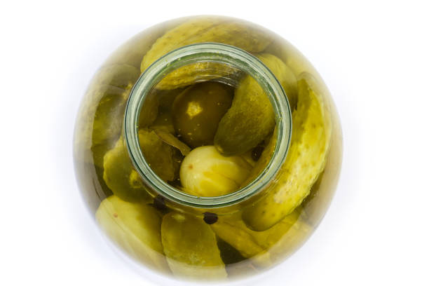 Canned cucumbers with spices in the open big glass jar, top view on a white background