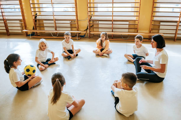 elementary school children sitting in circle in gym with teacher stock photo