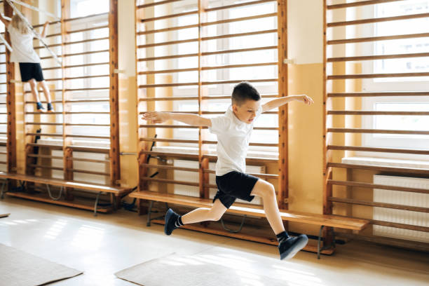 elementary schoolboy jumping in gym stock photo