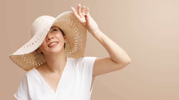 красивая азиатская женщина в шляпе от солнца улыбается и поднимает руку, чтобы блокировать солнечный свет - mature women portrait hat human face стоковые фото и изображения