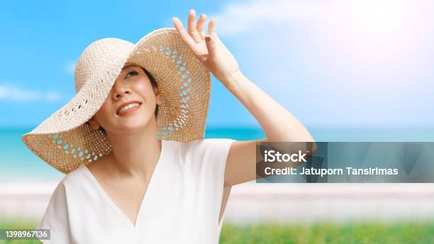 Beautiful Asian Woman Smiling And Raising Hand To Block Sunlight At The Beach Stock Photo - Download Image Now