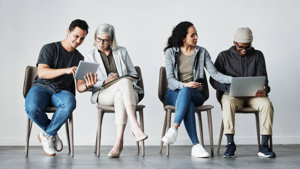 istock Businesspeople sitting in row using tech devices. Diverse businesspeople waiting for an interview, talking. Group of businesspeople collaborating. Business colleagues sitting in a line, planning 1398967760