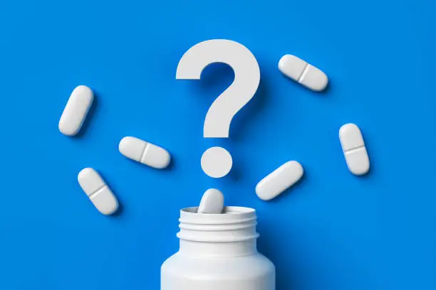 Photo of Plastic medical container and white capsule pills with question mark on blue background top view.