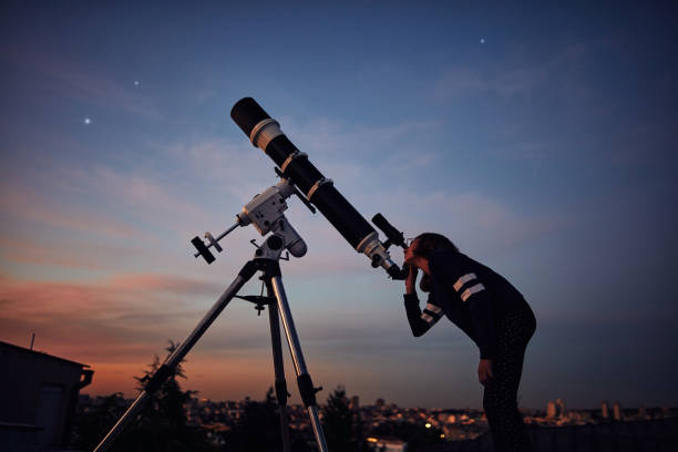 istock Girl with astronomical telescope stargazing under twilight sky. 1398968537