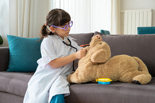 Little girl in doctor clothes examines her toy dog with toy stethoscope