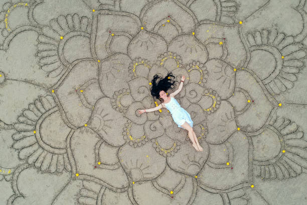 un grand mandala peint sur le sable sur l’océan avec une fille dans le style boho moyen. - women sarong beach white photos et images de collection