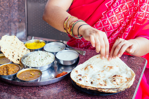 close up photo of Indian traditional vegetarian thali from rice, dal, potatoes, tomato salad on metal plate ,female hands roti india tortilla Chapati.